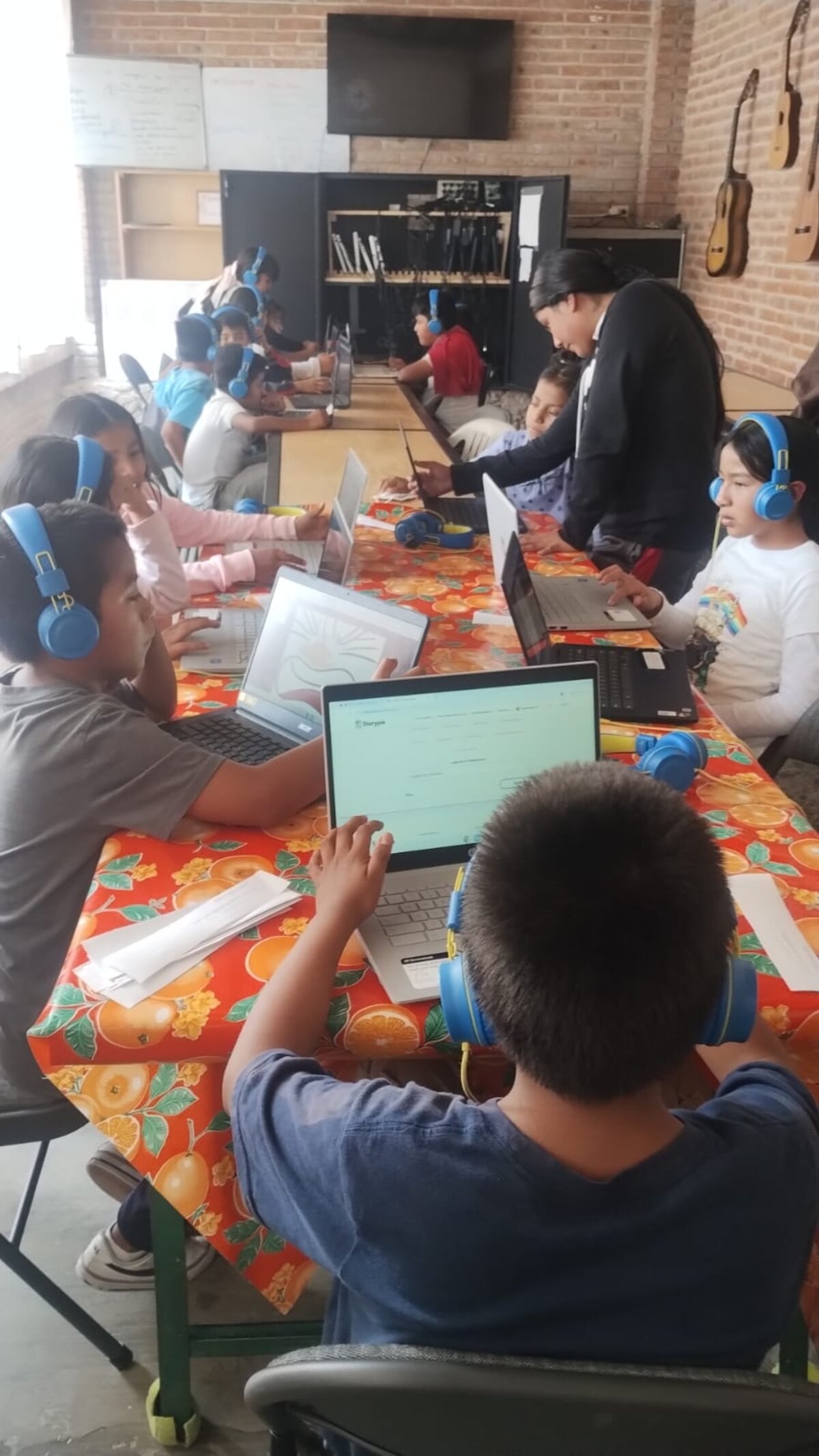 Bambini in una classe messicana che usano Storypie su laptop con cuffie blu.
